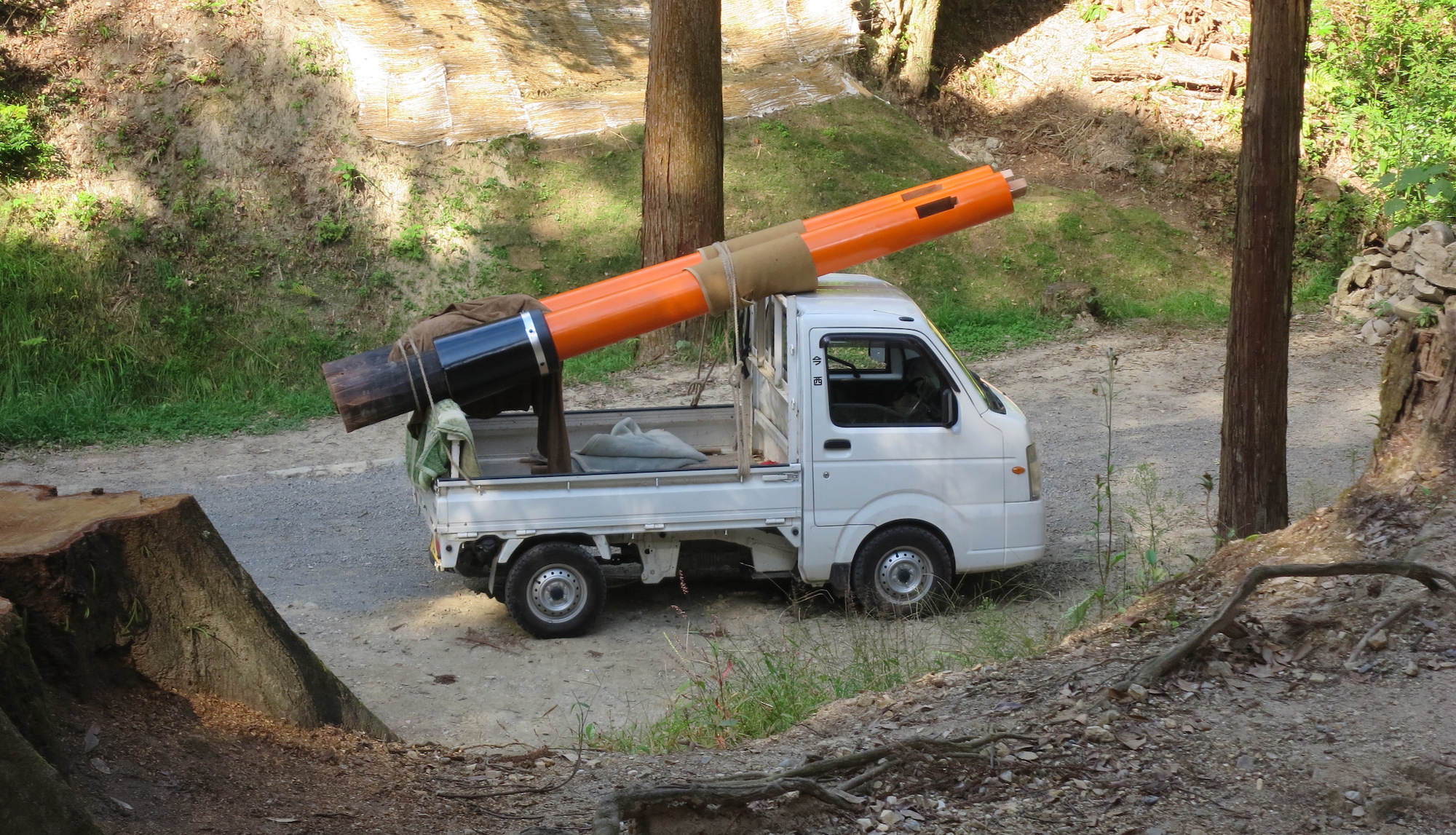 A part of a large torii gate is taken away for repair, on a tiny truck.